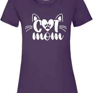 Peut inclure: T-shirt violet avec un motif blanc repr&eacute;sentant un visage de chat avec un c&oelig;ur et une empreinte de patte &agrave; l'int&eacute;rieur du c&oelig;ur et le texte "cat mom" en dessous.