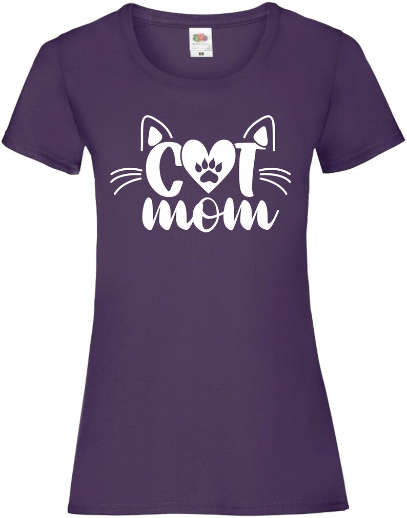 Peut inclure: T-shirt violet avec un motif blanc repr&eacute;sentant un visage de chat avec un c&oelig;ur et une empreinte de patte &agrave; l'int&eacute;rieur du c&oelig;ur et le texte "cat mom" en dessous.