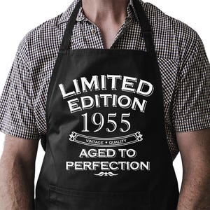 Könnte beinhalten: Schwarze Schürze mit weißem Text, der "Limited Edition 1955 Vintage Quality Gealtert zur Perfektion" lautet.