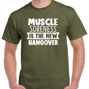 May include: A green t-shirt with white text that reads "Muscle Soreness Is The New Hangover".