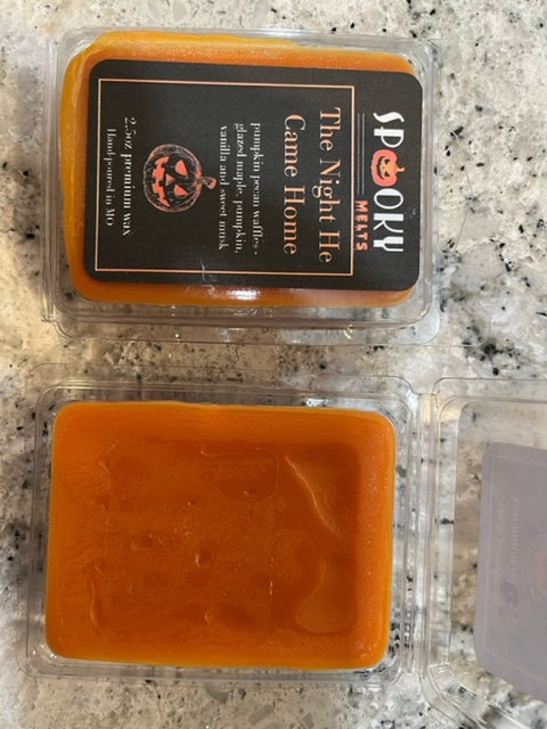May include: A 2.5 ounce candle in a clear plastic container with a black label that reads "Spooky Melts" and "The Night He Came Home". The candle is a pumpkin spice scent with notes of pecan waffles, glazed maple, pumpkin, vanilla, and sweet musk. The candle is hand-poured in Missouri.