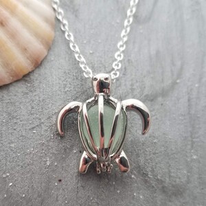 May include: Silver turtle necklace with a sea glass charm inside. The sea glass is a light green color.