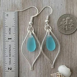 May include: Silver earrings with a teardrop-shaped turquoise blue glass bead hanging from each earring. The earrings are approximately 1 inch long.