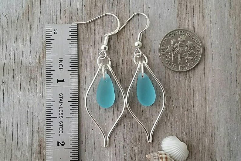 May include: Silver earrings with a teardrop-shaped turquoise blue glass bead hanging from each earring. The earrings are approximately 1 inch long.
