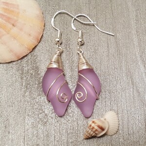 May include: A pair of silver earrings with lavender glass teardrop shapes wrapped in silver wire. The wire is twisted into a spiral design.