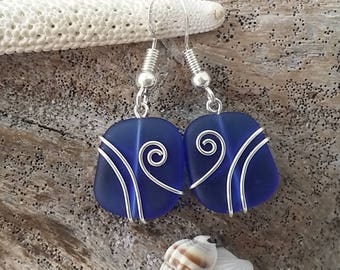 May include: A pair of blue sea glass earrings with silver wire wrapped around the glass. The wire has a swirl design.