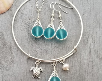 May include: A silver bangle bracelet with a turquoise sea glass charm, a silver turtle charm, a pearl charm, and a pair of turquoise sea glass earrings.