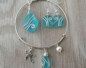 May include: A silver bangle bracelet with a blue sea glass charm, a starfish charm, a pearl charm, and a second blue sea glass charm. Matching blue sea glass earrings with silver wire accents.