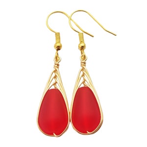 May include: A pair of gold dangle earrings with red teardrop-shaped glass beads. The beads are encased in a gold wire cage.
