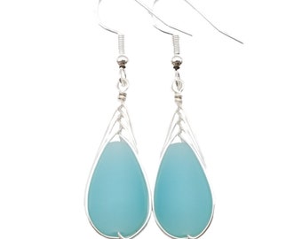 May include: A pair of silver-toned drop earrings with a teardrop shape. Each earring features a light blue, opaque stone encased in a delicate, openwork silver frame. The earrings have a simple hook closure.