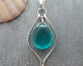May include: A teal sea glass pendant necklace with a silver wire frame. The pendant is shaped like a teardrop and hangs from a silver chain.