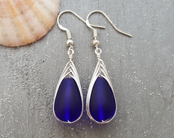 May include: A pair of silver teardrop earrings with dark blue glass beads. The beads are encased in a silver wire cage.
