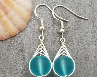 May include: A pair of silver dangle earrings with a turquoise blue glass bead in each. The beads are encased in a silver wire cage.