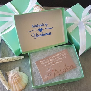 May include: A light green gift box with a white ribbon and a card that says "Mahalo for spreading the "Hawaii Aloha" with this handmade jewelry by yinahawaii Aloha". The box is open and the inside is lined with white tissue paper.