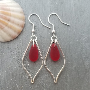 May include: A pair of silver dangle earrings with a red glass teardrop pendant on each earring.