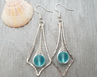 May include: A pair of silver dangle earrings with a turquoise blue glass bead in each. The earrings have a geometric design.