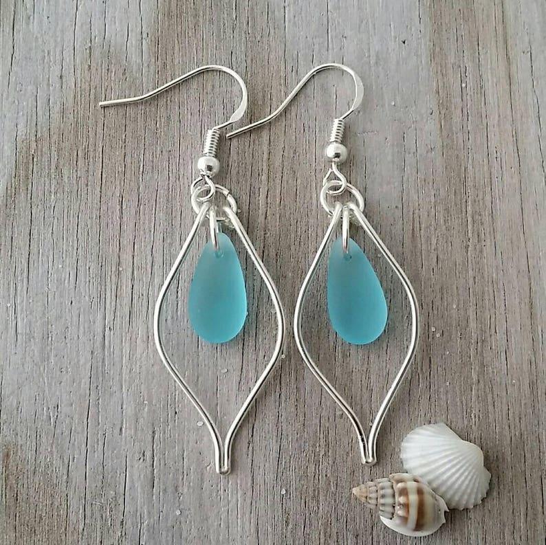 May include: A pair of silver earrings with a teardrop-shaped piece of turquoise blue sea glass hanging from each earring.