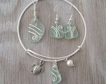 May include: A silver bangle bracelet with a sea turtle charm, a pearl charm, and a sea glass charm. The bracelet also comes with a matching sea glass necklace and earrings.