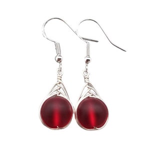 May include: A pair of silver dangle earrings with a red glass bead in each. The beads are encased in a silver wire cage.