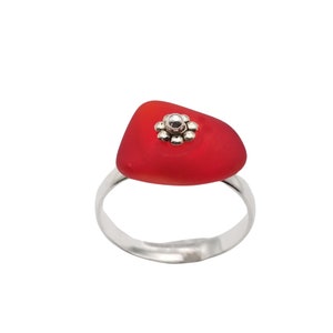 May include: A silver ring with a red, triangular sea glass stone and a silver flower design.
