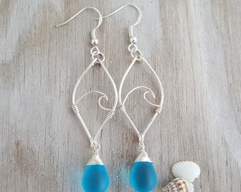 May include: Silver wire earrings with a wave design and a teardrop-shaped blue glass bead hanging from each earring.