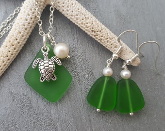 May include: A set of sea glass jewellery featuring a green sea glass pendant with a silver turtle charm and a pearl, and a pair of green sea glass earrings with pearls.
