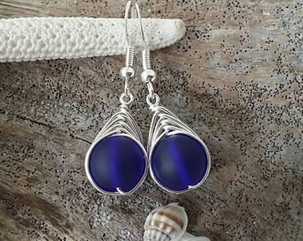 May include: A pair of silver dangle earrings with a dark blue glass bead in each. The beads are surrounded by silver wire.