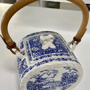 May include: A blue and white porcelain teapot with a bamboo handle. The teapot features a floral pattern and a scene of a countryside landscape.
