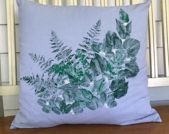 May include: A square, light blue pillow with a botanical design. The design features green fern and leaf prints with small white accents. The pillow is made of a soft fabric and is suitable for home decor.