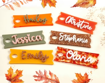 May include: Six colourful acrylic name tags with rounded edges and holes for hanging. The tags feature the names Hailey, Christine, Jessica, Stephanie, Emily, and Olivia in white and pink lettering.