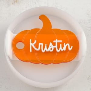 May include: Orange pumpkin-shaped acrylic ornament with the name "Kristin" written in white lettering.