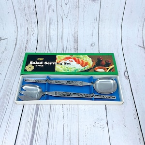 May include: A two-piece salad serving set in a green and blue box. The set includes a serving spoon and a serving fork with a vine design. The box has a picture of a salad and the text "YAK Salad Serving Set 2 PIECE".