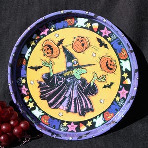 May include: A round Halloween-themed tray with a purple rim and a yellow center. The tray features a cartoon witch juggling jack-o'-lanterns, bats, stars, and candy corn. The tray is a decorative item.