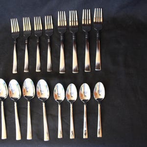 May include: A collection of silverware, including forks and spoons, arranged on a black surface. The forks have a two-tone design with a silver tine and a brown handle. The spoons have a silver bowl and a silver handle.