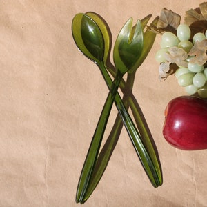 May include: A set of green salad serving utensils, a red apple, and a bunch of green grapes on a brown paper background.