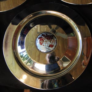 Puede incluir: Juego de platos decorativos con borde dorado y anillo exterior negro. El centro de cada plato presenta un dise&ntilde;o de globo terr&aacute;queo con continentes rojos y blancos. Los platos est&aacute;n dispuestos sobre una superficie oscura.