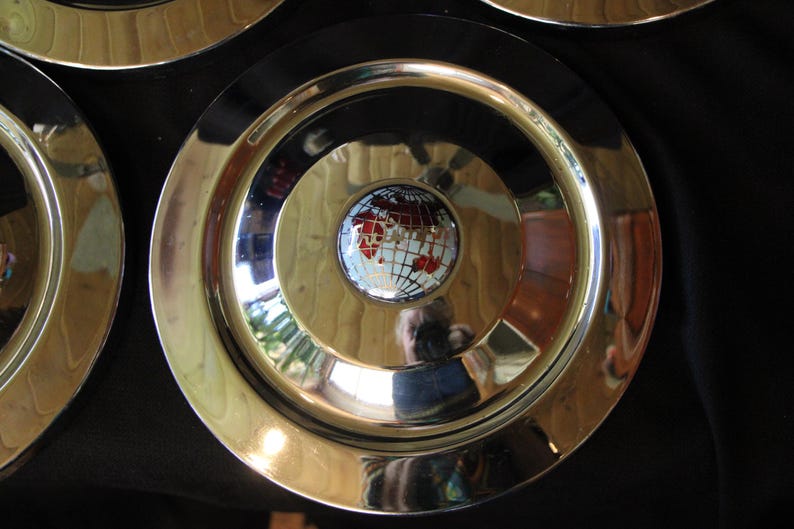 Puede incluir: Juego de platos decorativos con borde dorado y anillo exterior negro. El centro de cada plato presenta un dise&ntilde;o de globo terr&aacute;queo con continentes rojos y blancos. Los platos est&aacute;n dispuestos sobre una superficie oscura.