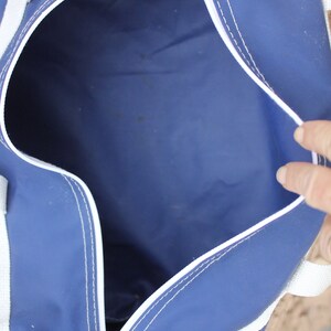 May include: A blue duffel bag with white trim and a zipper opening. The bag is empty and the inside is visible.