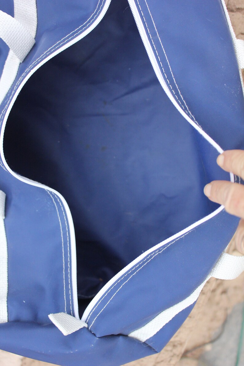 May include: A blue duffel bag with white trim and a zipper opening. The bag is empty and the inside is visible.
