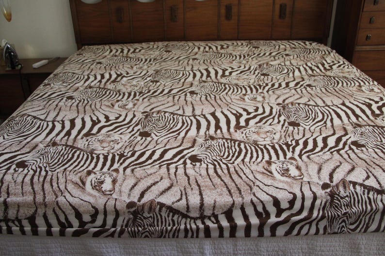 Puede incluir: Una s&aacute;bana con un patr&oacute;n repetitivo de cebras y tigres en color marr&oacute;n y blanco. El dise&ntilde;o muestra m&uacute;ltiples animales superpuestos en la tela, donde las rayas marr&oacute;n oscuro de las cebras y los patrones de pelaje de tigre crean un efecto visual denso.