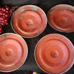 Puede incluir: Cuatro tapas met&aacute;licas rojas vintage con dise&ntilde;os de c&iacute;rculos conc&eacute;ntricos y bordes plateados est&aacute;n dispuestas sobre una superficie negra. Un racimo de uvas rojas est&aacute; en la esquina superior izquierda. Las tapas parecen ser de una olla o sart&eacute;n.