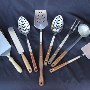 May include: A set of eight kitchen utensils with wooden handles. The utensils include a slotted spoon, a spatula, a ladle, a fork, and three spatulas.