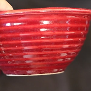 May include: A red ceramic bowl with a ribbed design. The bowl is empty and has a glossy finish.