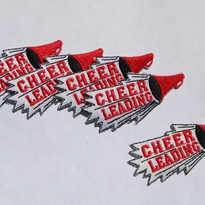 May include: Five red and white embroidered iron-on patches with a megaphone design and the text "Cheer Leading" in red.
