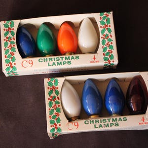 May include: Two rectangular cardboard boxes containing C9 Christmas lamps. Each box holds four bulbs with metallic bases. The first box features blue, green, orange, and white bulbs. The second box contains white, blue, blue, and dark red bulbs.
