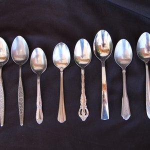 May include: Eight silver spoons with varying designs on a black background. The spoons are all polished and reflect light.
