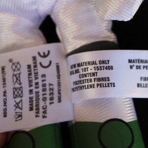 May include: White fabric label with black text that reads "ALL NEW MATERIALS Polyester Fibers, Polyethylene Pellets REG.NO.PA-13401 [V FABRIQUE EN VIETNAM MADE IN VIETNAM FAC-018813 16327 CE GRC D10314040001 NEW MATERIAL ONLY REG.NO. 10T - 1537408 CONTENT POLYESTER FIBRES POLYETHYLENE PELLETS MAT&Eacute;RIAUX NEUFS SEULEMENT N&deg; DE PERMIS: 10T - 1537408 CONTENU FIBRES DE POLYESTER BILLES DE POLYETHYLENE"