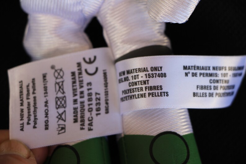May include: White fabric label with black text that reads "ALL NEW MATERIALS Polyester Fibers, Polyethylene Pellets REG.NO.PA-13401 [V FABRIQUE EN VIETNAM MADE IN VIETNAM FAC-018813 16327 CE GRC D10314040001 NEW MATERIAL ONLY REG.NO. 10T - 1537408 CONTENT POLYESTER FIBRES POLYETHYLENE PELLETS MAT&Eacute;RIAUX NEUFS SEULEMENT N&deg; DE PERMIS: 10T - 1537408 CONTENU FIBRES DE POLYESTER BILLES DE POLYETHYLENE"