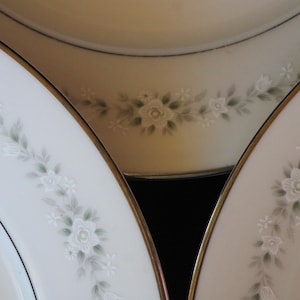 May include: Three white ceramic plates with gold trim and a floral design. The plates are stacked on top of each other.