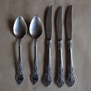 May include: Set of five silver-plated utensils, including two spoons and three knives. The utensils have ornate, floral designs on the handles.